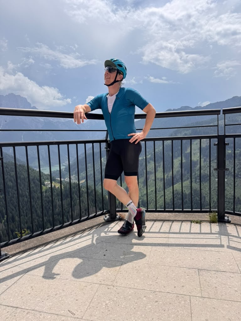 Guide in cycling kit leaning on a railing above an alpine valley in the Dolomites