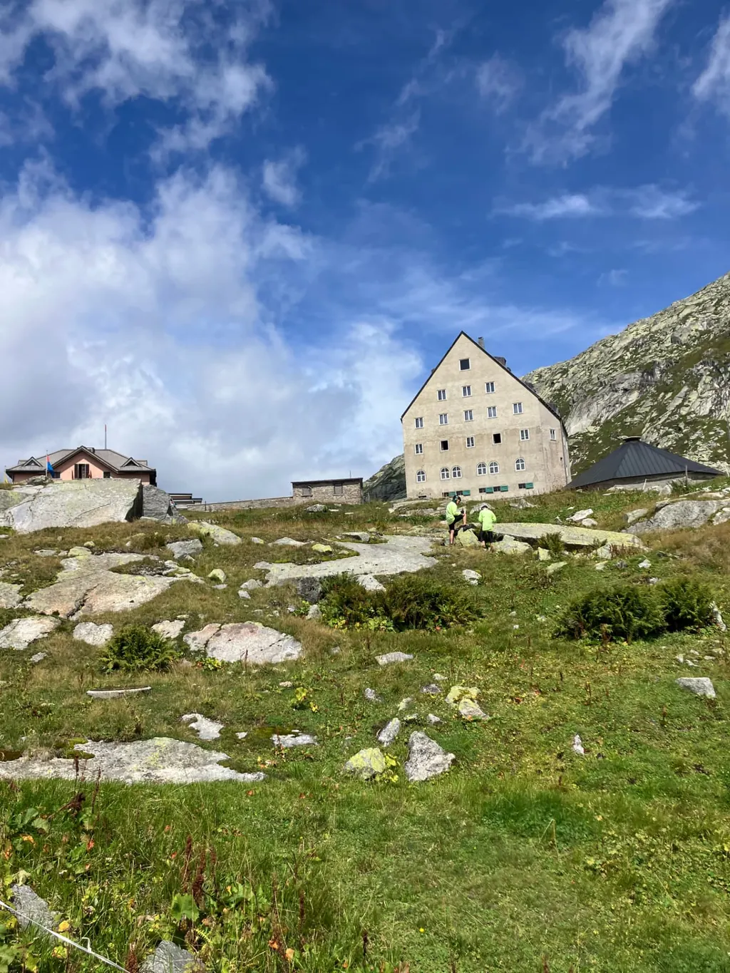 Cyclists resting below the historic Ospizio San Gottardo hospice at the Gotthard summit