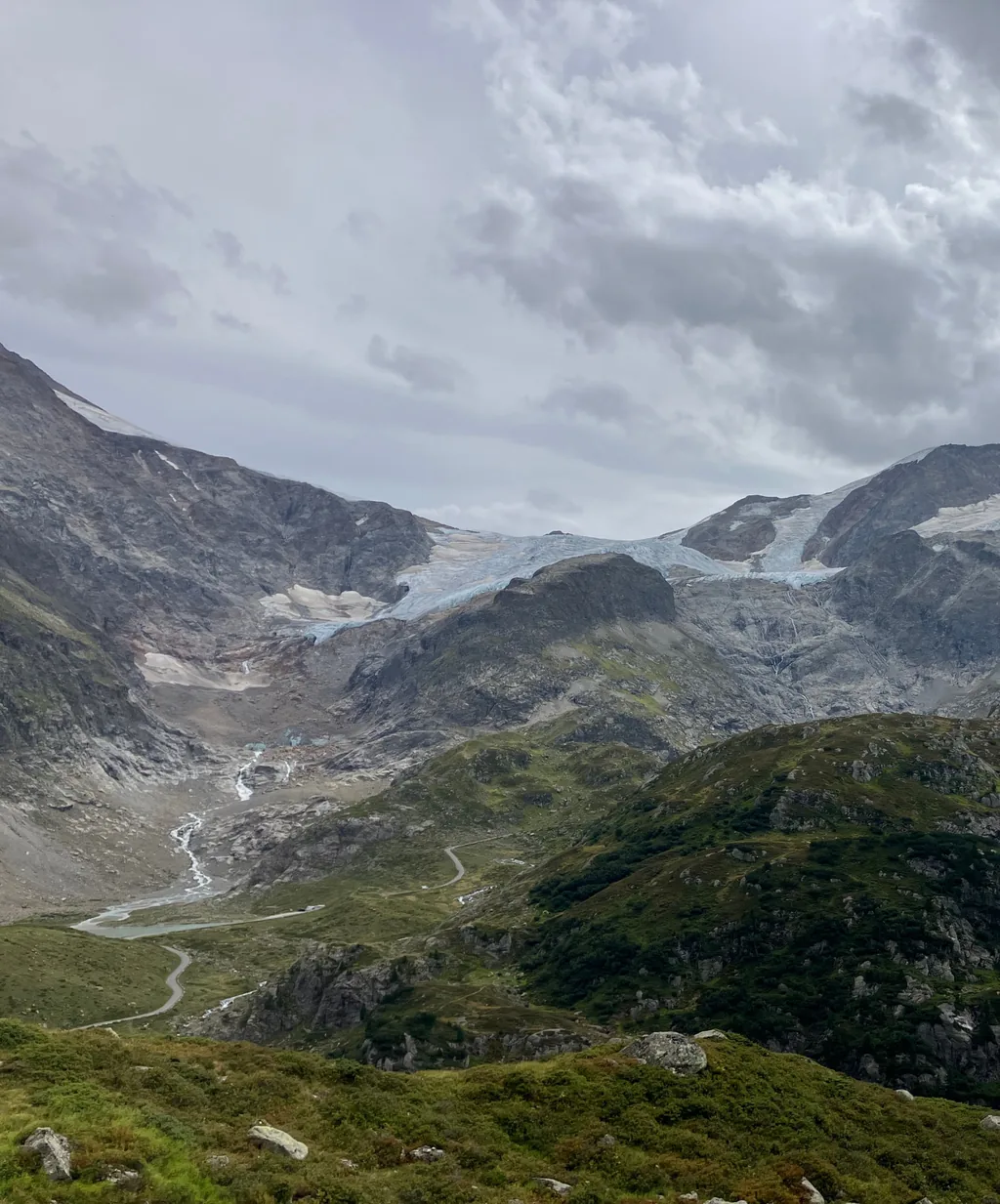 The Steingletscher draped over rocky peaks under heavy clouds, its glacial stream winding down to a small turquoise tarn above the Sustenpass road